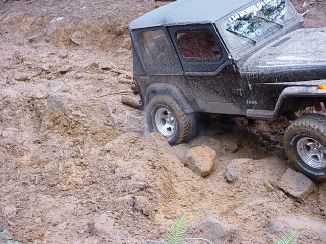 Black 1995 Jeep Wrangler navigating a rocky, muddy off-road trail