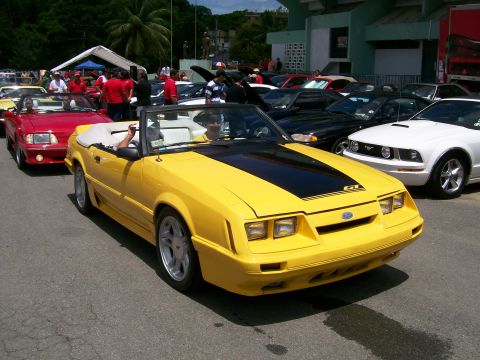 2001 Ford Mustang - A yellow convertible Mustang GT is parked in a lot with other vehicles.