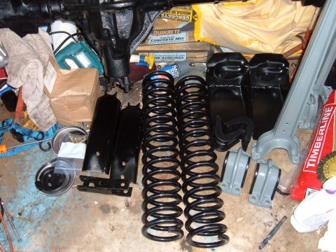 1995 Ford Bronco - Various automotive suspension components are organized on a concrete floor, ready for installation.