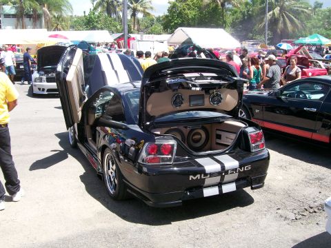 2001 Ford Mustang - A black Ford Mustang with custom audio equipment and unique doors is displayed at an outdoor car show.