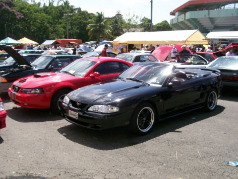 2001 Ford Mustang - A black convertible Mustang, likely from the mid-1990s, is displayed at an outdoor car show alongside other vehicles.