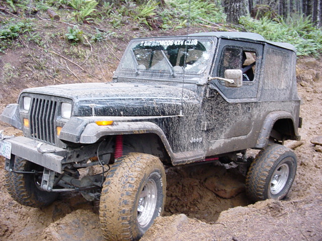 Mud-covered Jeep Wrangler off-roading on a dirt trail