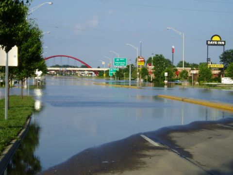 1995 Mercury Grand Marquis - A road is submerged in floodwaters, with a red bridge and a Days Inn visible in the background.