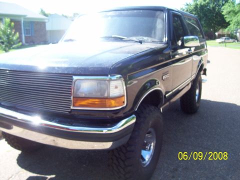 1994 Ford Bronco - A dark-colored Ford Bronco is shown from the front-right side, parked on a residential street.