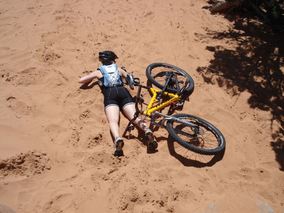 Cyclist lying in red sand after crashing, yellow mountain bike on top of her legs
