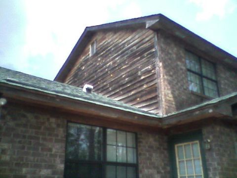 1992 Ford F-150 - Upward view of a house gable end clad in weathered diagonal wood siding above a brown brick lower story, with shingled roof, gutter and a g…