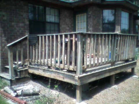 1992 Ford F-150 - Weathered ground-level wood deck with a spindle railing and open post framing underneath, attached to a brown brick house with a glass-pane…