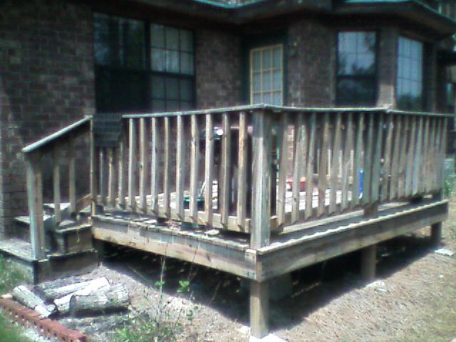 Weathered wood ground-level deck with railing attached to a brick house
