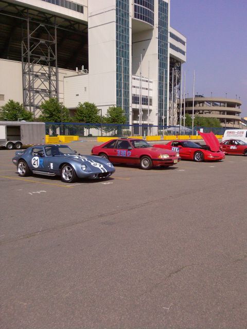 2001 Mercury Grand Marquis - Several cars, including a blue Shelby Cobra replica and red Ford Mustang, are parked in a lot near a stadium.
