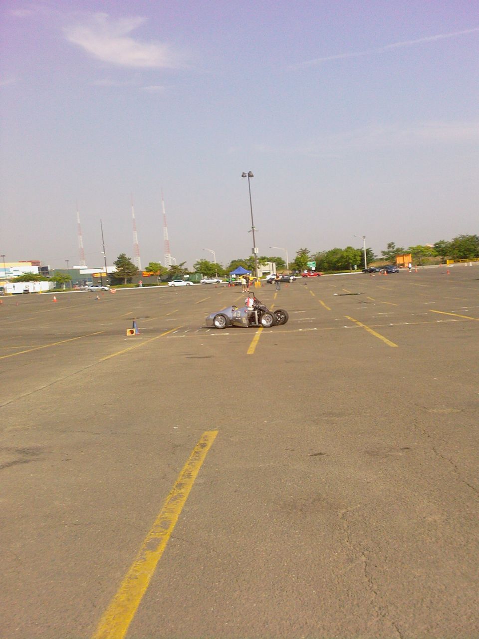 Driver in a custom open-wheel race car on a paved lot with cones
