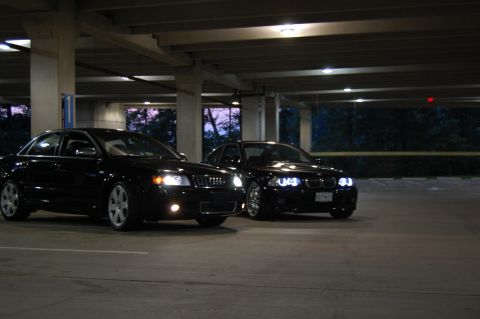 2002 BMW M3 - Two black sedans, an Audi and a BMW, are parked side-by-side in a dimly lit parking structure.