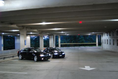 2002 BMW M3 - Two black sedans are parked in a dimly lit parking garage with trees visible in the background.