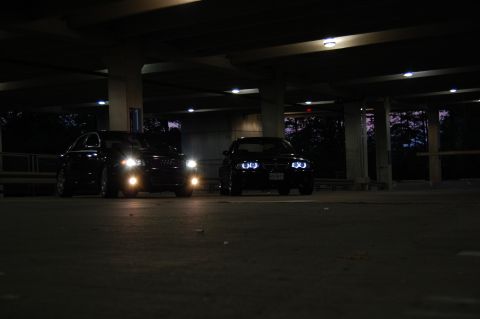 2002 BMW M3 - Two black cars are parked under a bridge at night, with their headlights illuminated.