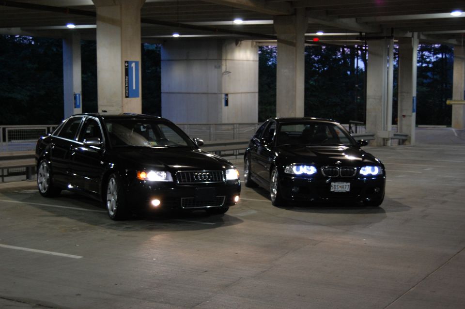 Two black sedans parked in a garage. One is an Audi, the other is a BMW