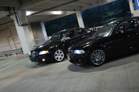 2002 BMW M3 - Two black sedans, including a 2002 BMW M3, are parked in a dimly lit garage with concrete pillars and overhead lighting.