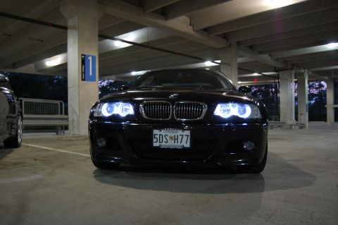 2002 BMW M3 - A black 2002 BMW M3 sedan is viewed from the front in a parking garage with its distinctive halo headlights illuminated.