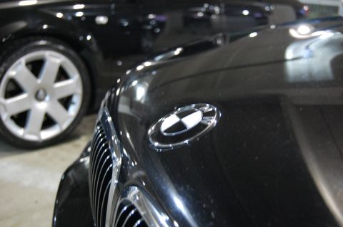 2002 BMW M3 - Front view of a black BMW showing the hood emblem and grille. Another car is visible in the background.