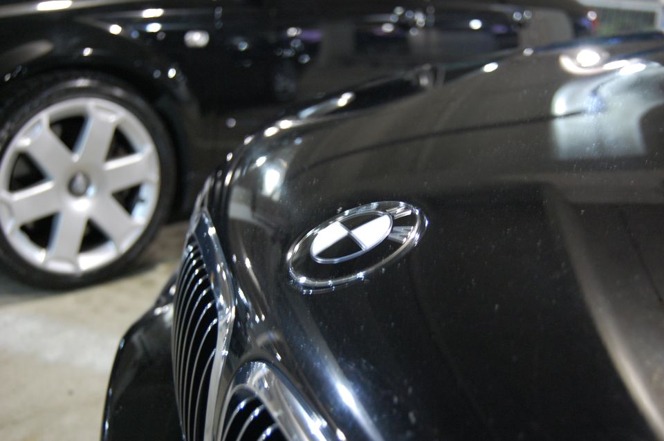 Close-up of black BMW hood emblem and grille, with another black car and its wheel in the background