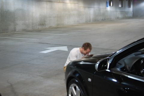2002 BMW M3 - A man inspects the hood of a black 2002 BMW M3 parked in a dimly lit concrete garage.