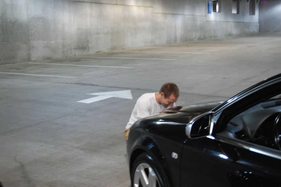 Black 2002 BMW M3 with a man bending over the hood in a concrete parking garage