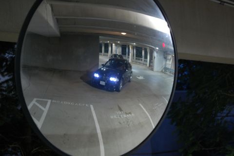 2002 BMW M3 - A dark sedan is visible in a parking garage, its headlights illuminated.