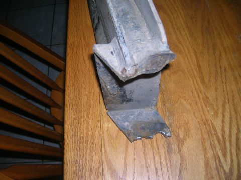 1996 Ford Bronco - Close-up of a damaged metal component, likely a vehicle part, resting on a wooden surface.