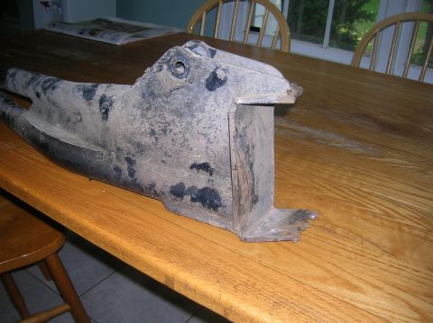 1996 Ford Bronco - A dirty, black metal vehicle suspension part rests on a wooden table.