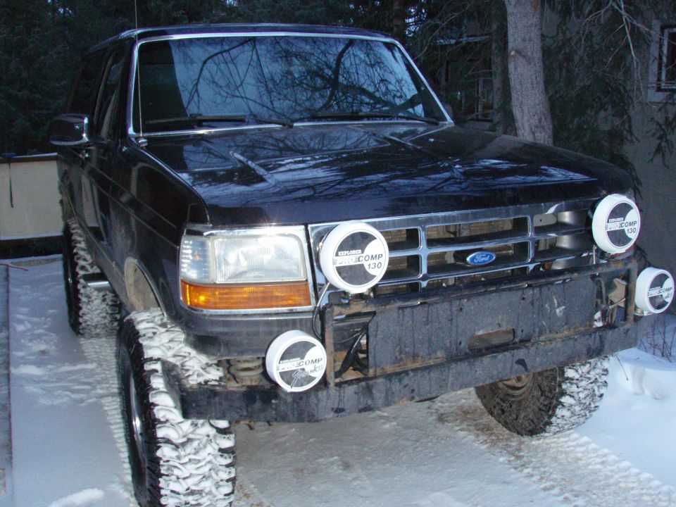 Black lifted Ford Bronco in snow with four Pro Comp driving lights on the grille