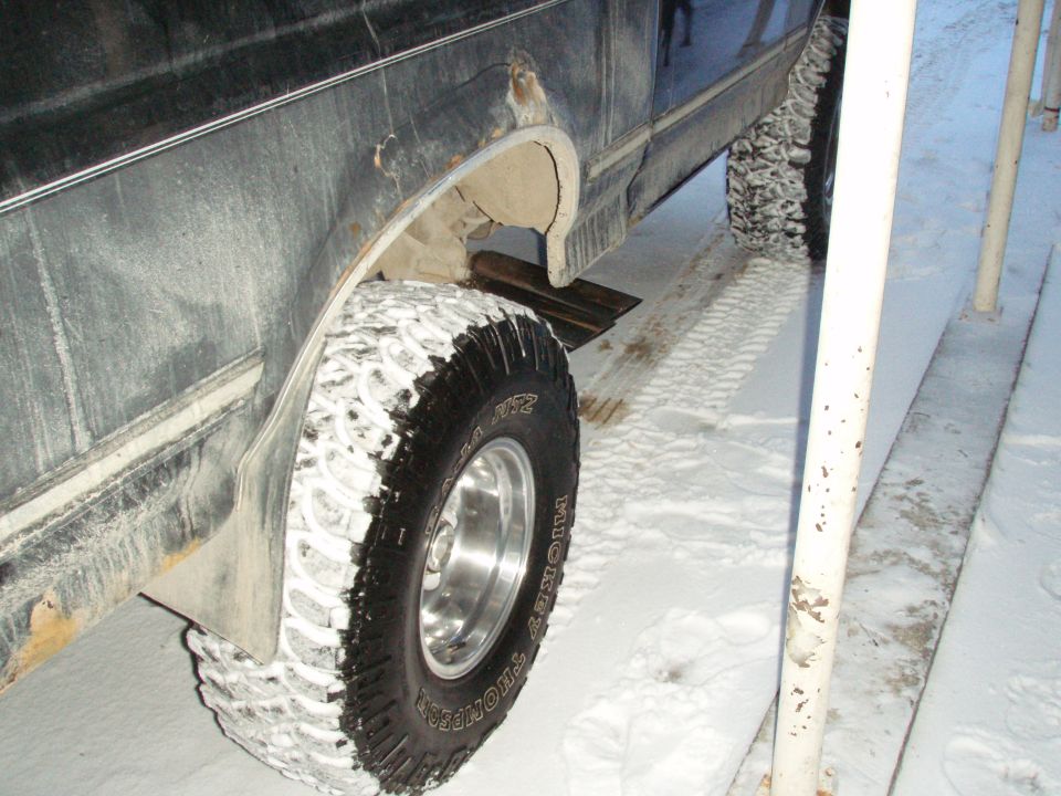 Trimmed rear fender arch and snow-packed Mickey Thompson MTZ tire on a dark Ford