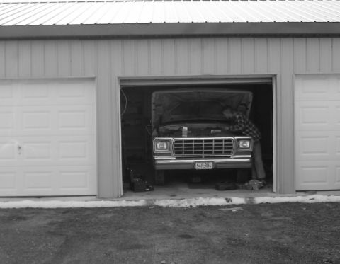 1979 Ford F-100 - Person working on the engine of a 1979 Ford F-100 truck parked inside a garage.