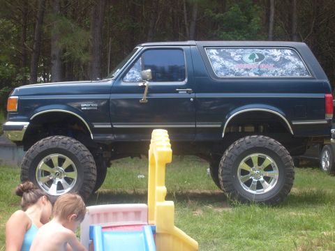 1989 Ford Bronco - A lifted 1989 Ford Bronco is shown in a side profile, with children playing nearby.