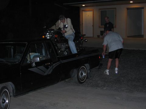 1985 Ford LTD Crown Victoria - A motorcycle is being loaded into the bed of a black pickup truck at night.