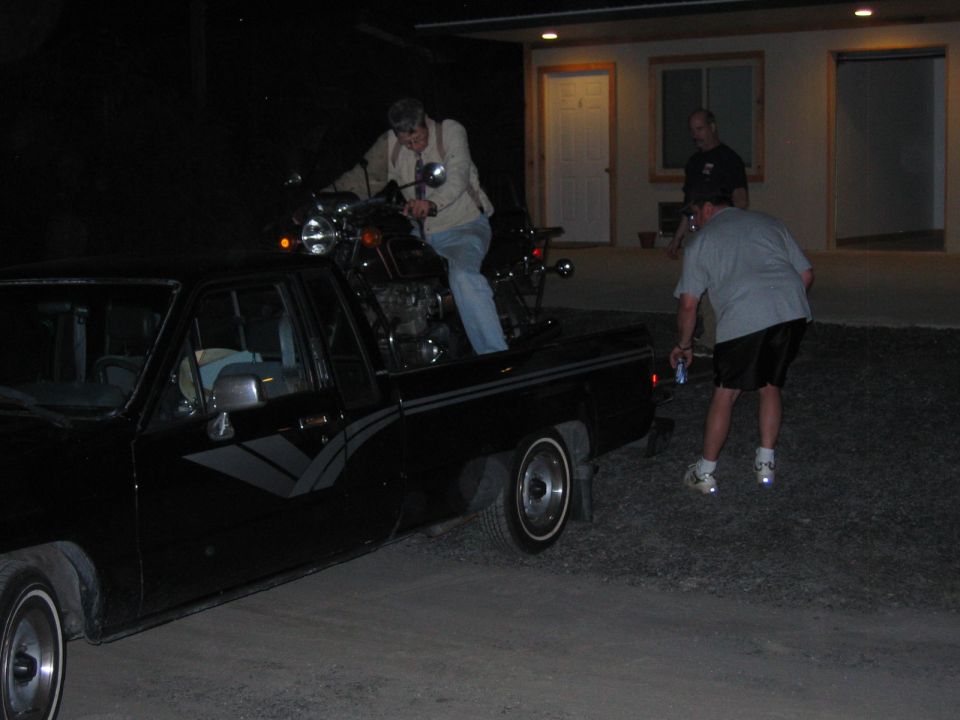 Black pickup truck with a motorcycle being loaded into its bed, two men nearby
