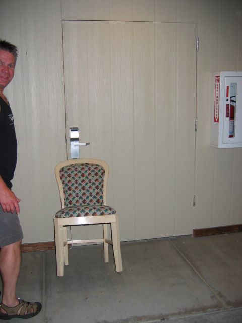 1985 Ford LTD Crown Victoria - A man stands beside a chair in front of a door, with a fire extinguisher visible on the wall.