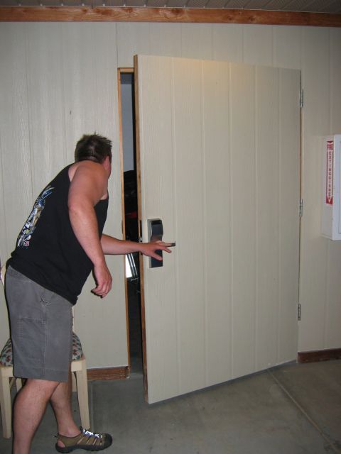 1985 Ford LTD Crown Victoria - A man reaches for the handle of a partially open beige door, with a fire extinguisher mounted on the wall to the right.