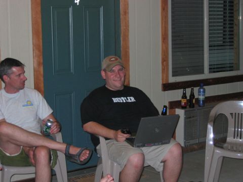 1985 Ford LTD Crown Victoria - Two men relax outdoors with a laptop and beverages near a doorway.