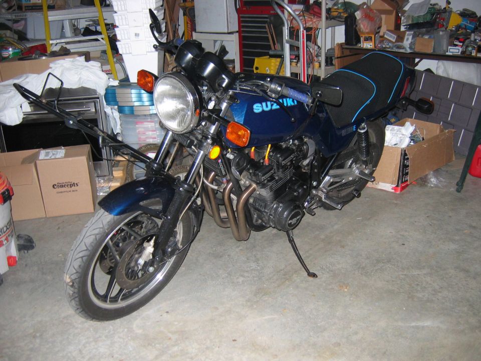 Blue Suzuki motorcycle parked in a garage with boxes and shelves in the background