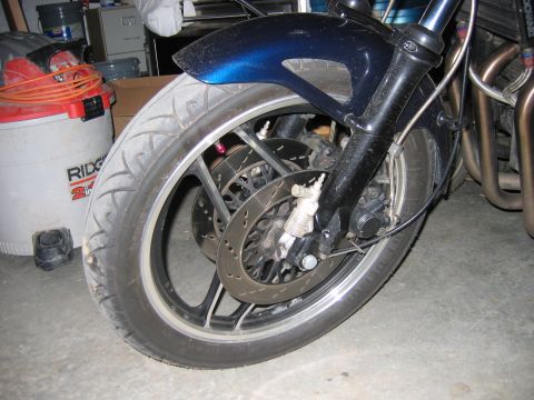1985 Ford LTD Crown Victoria - Close-up of a motorcycle's front wheel, suspension, and exhaust pipes.