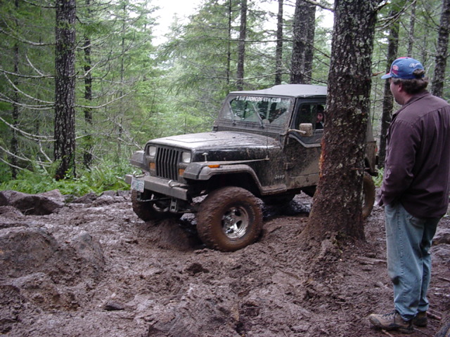 1995 Jeep Wrangler stuck in mud on a wooded trail, person standing nearby