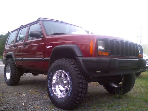 1998 Jeep Cherokee - A lifted 1998 Jeep Cherokee with custom wheels and tires is parked outdoors on a gravel surface.