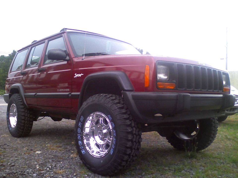 Red 1998 Jeep Cherokee with lifted suspension and chrome wheels. "Sport" and "Cherokee" badges are visible