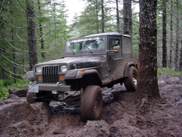 Mud-covered Jeep Wrangler on a muddy trail, front-left tire angled up