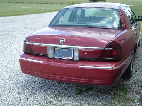 1999 Mercury Grand Marquis - Rear view of a red sedan parked on a gravel road with a grassy background.
