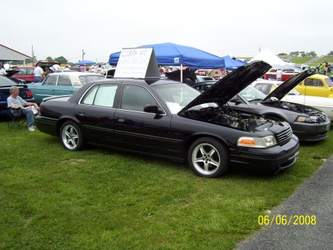 2008 Ford Crown Victoria - A black 2008 Ford Crown Victoria is displayed with its hood open, alongside other vehicles at an outdoor gathering.