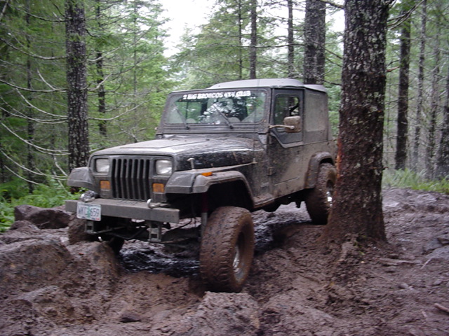 Muddy Jeep Wrangler YJ with hardtop crawling a rutted forest mud trail