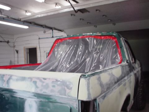 1996 Ford Bronco - pickup truck bed undergoing bodywork in a garage, sanded to primer with the bed opening masked in plastic.