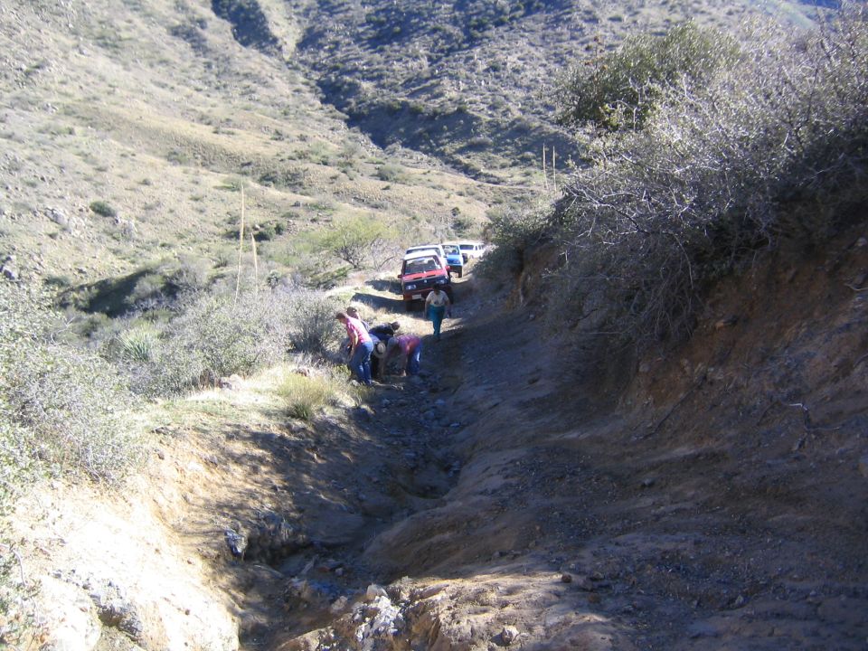 Vehicles parked on a rugged eroded mountain dirt trail with people working nearby