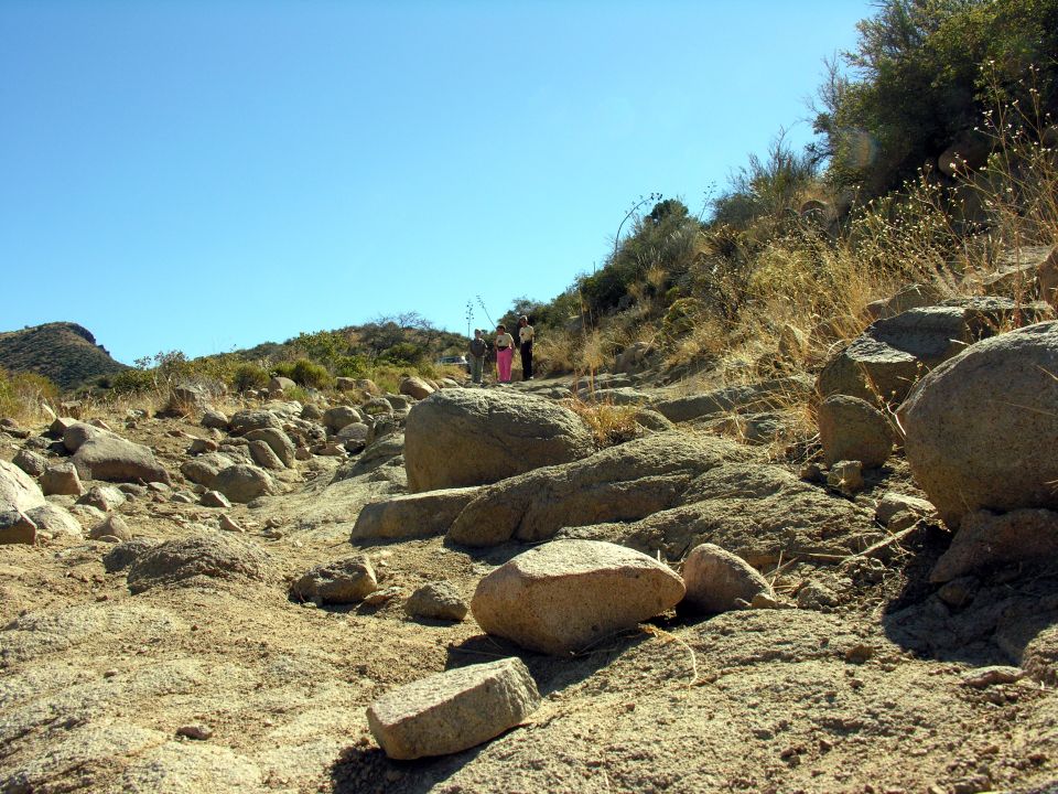 Rocky dry trail with boulders and distant people under blue sky