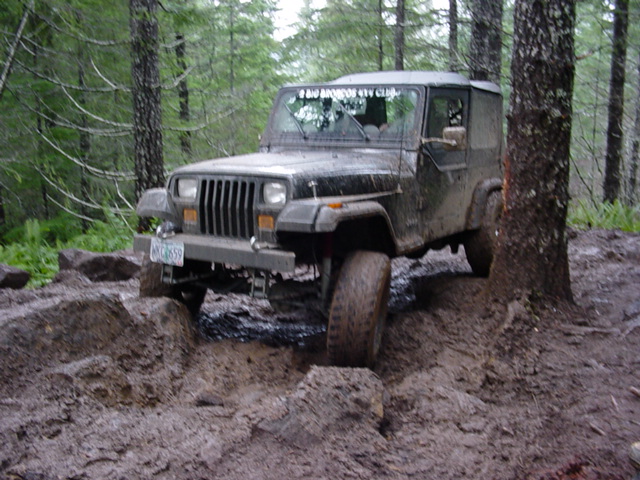 Black Jeep Wrangler on a muddy trail, front 3/4 view