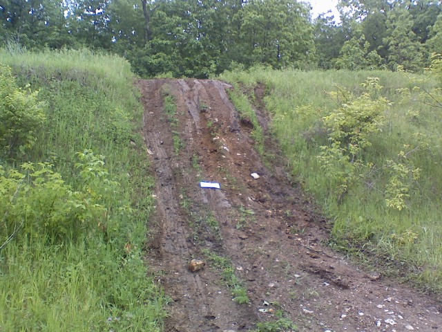 Steep rutted dirt trail cut into a grassy green hillside